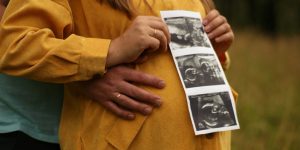 woman in brown coat holding picture of man in black shirt
